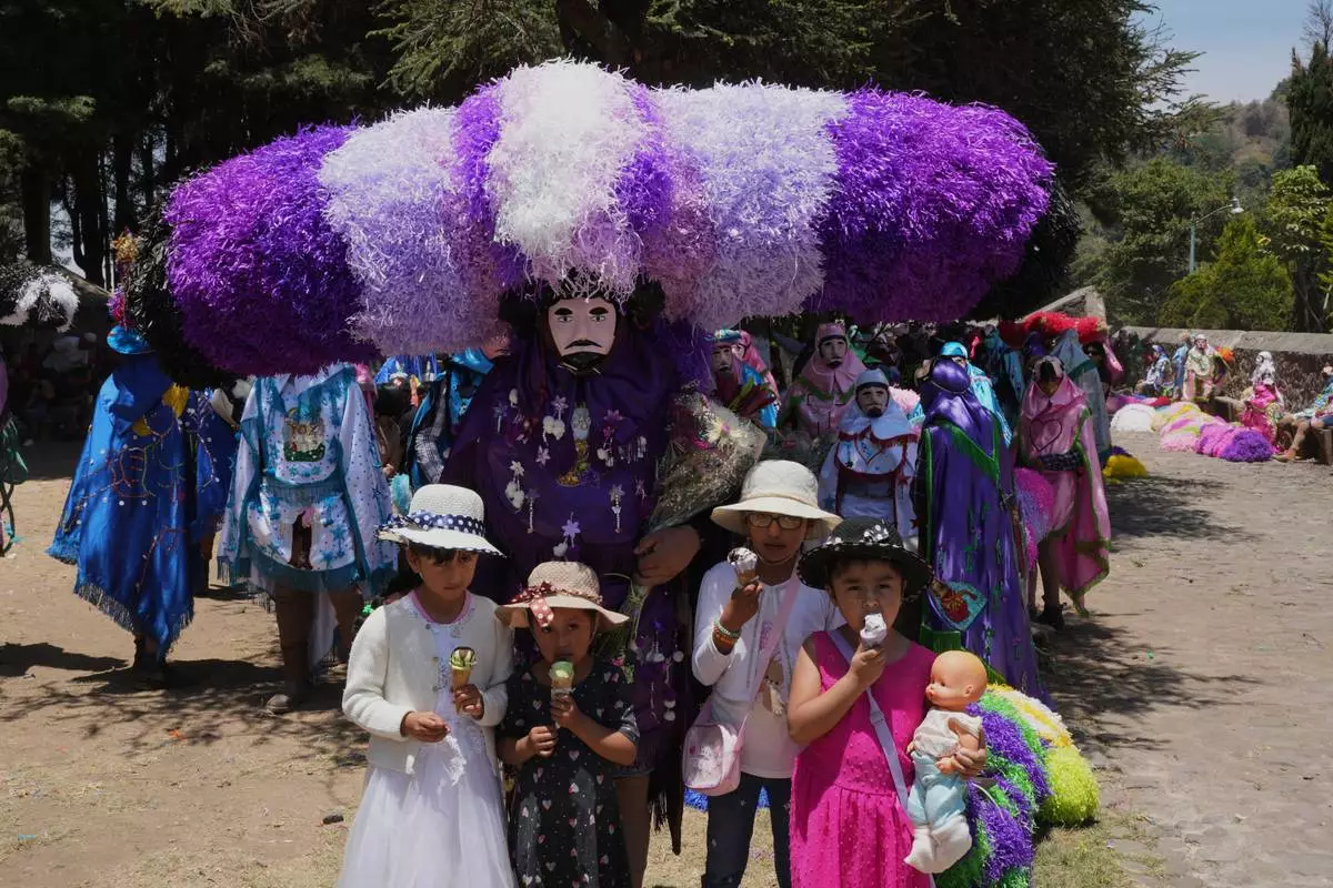 Children pose for a photo with a reveler, known as a sayon, in a tissue paper hat during Easter Day celebrations in Tetela del Volcan, Mexico, Sunday, April 20, 2025. (AP Photo/Eduardo Verdugo)