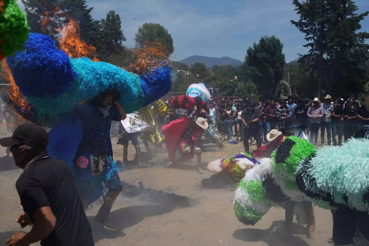 Revelers, known as a sayones, try to put out fires they started on tissue paper hats as part of Easter celebrations in Tetela del Volcan, Mexico, Sunday, April 20, 2025. (AP Photo/Eduardo Verdugo)