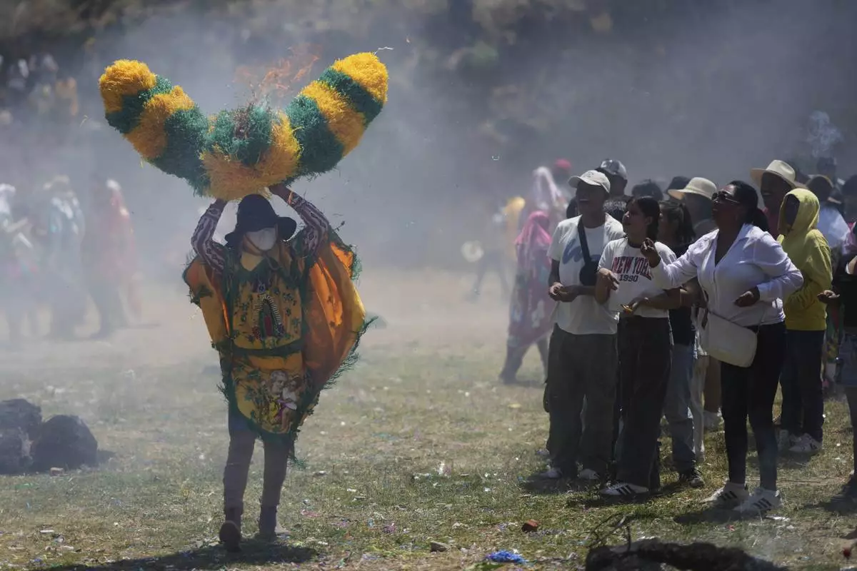 Onlookers throw lit matches at a reveler, known as a sayon, wielding a tissue paper hat during Easter celebrations in Tetela del Volcan, Mexico, Sunday, April 20, 2025. (AP Photo/Eduardo Verdugo)