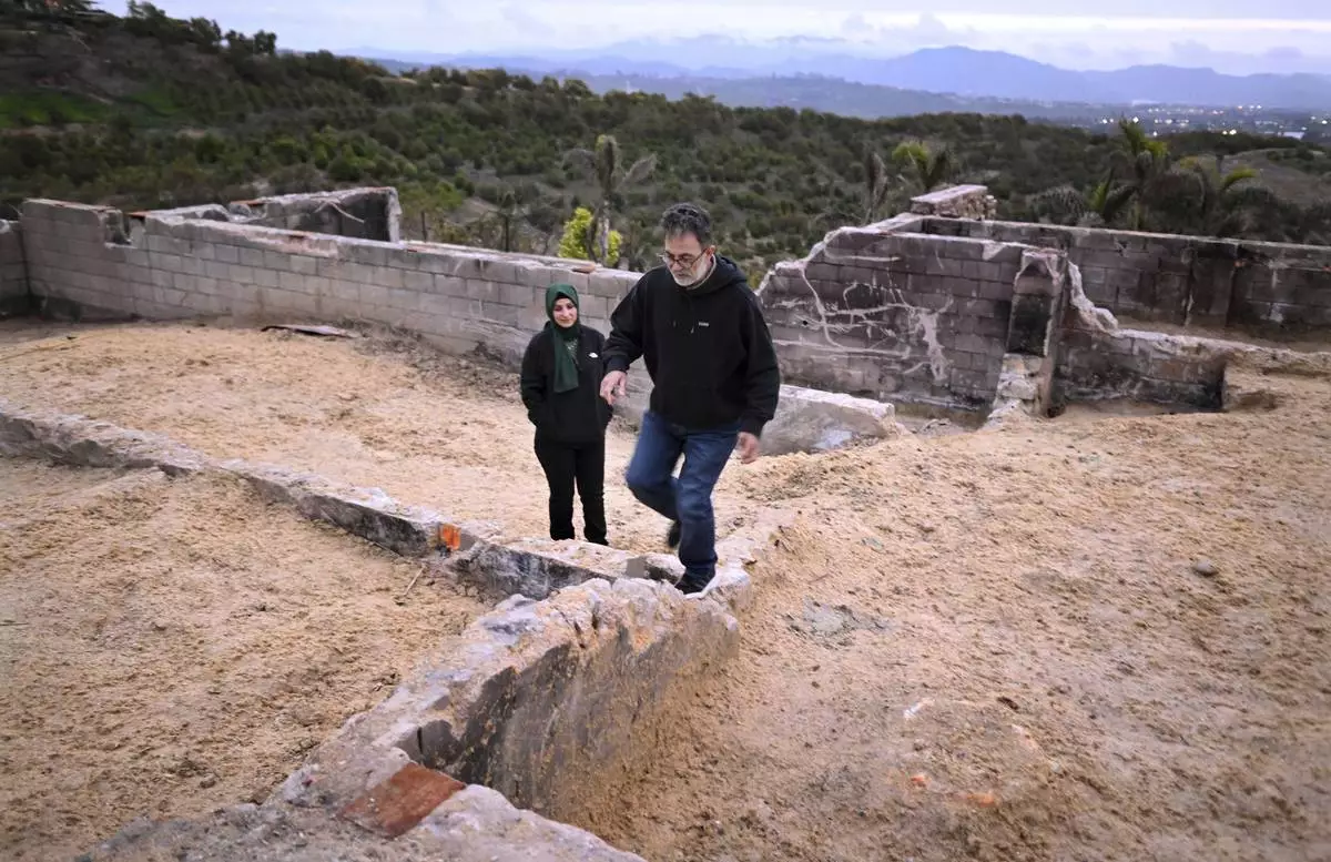 Hatim Naim and his wife Samah walk in the ruins of their property which burned in the Mountain Fire Wednesday, April 16, 2025, in Somis, Calif. (AP Photo/Wally Skalij)