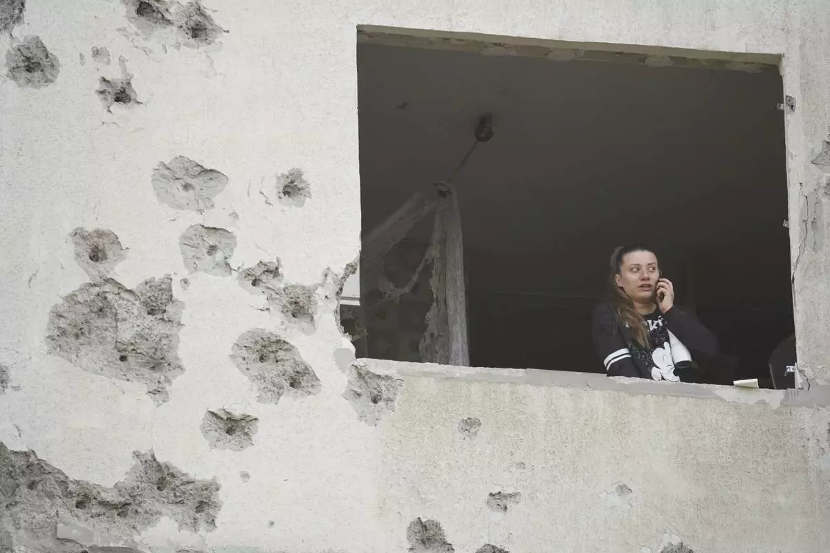A woman looks though the window of her damaged apartment following a Russian strike in Kharkiv, Ukraine, Friday April 18, 2025. (AP Photo/Andrii Marienko)