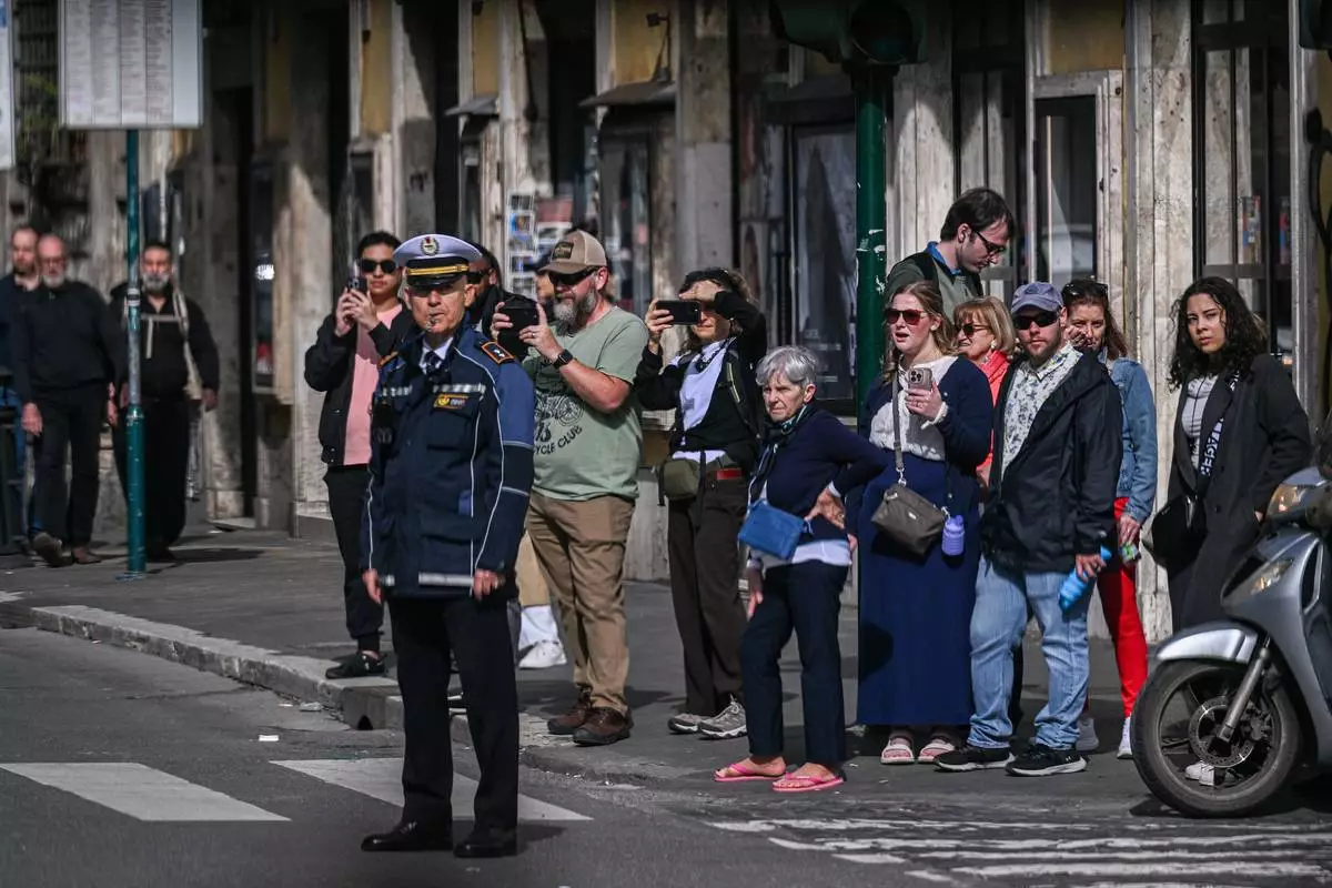 People look on as the motorcade of U.S. Vice President JD Vance passes by en route to Vatican where Vance will meet with Cardinal Pietro Parolin and Archbishop Paul Gallagher, in Rome, Italy, Saturday, April 19, 2025. (Kenny Holston/Pool Photo via AP)