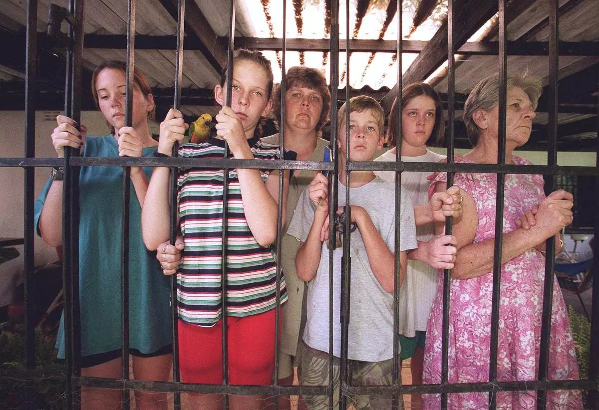 FILE - From left: Katrina Liebenberg,17, together with her cousin Natalie van Staden, Natalie's mother Maria, brother Chad, 11, sister Lee-Ann, 17, and grandmother Aletta, on the back verandah of the farm cottage, March 2, 2000, where they have been besieged for four days by Zimbabwe War Veterans. (AP Photo/Rob Cooper, file)