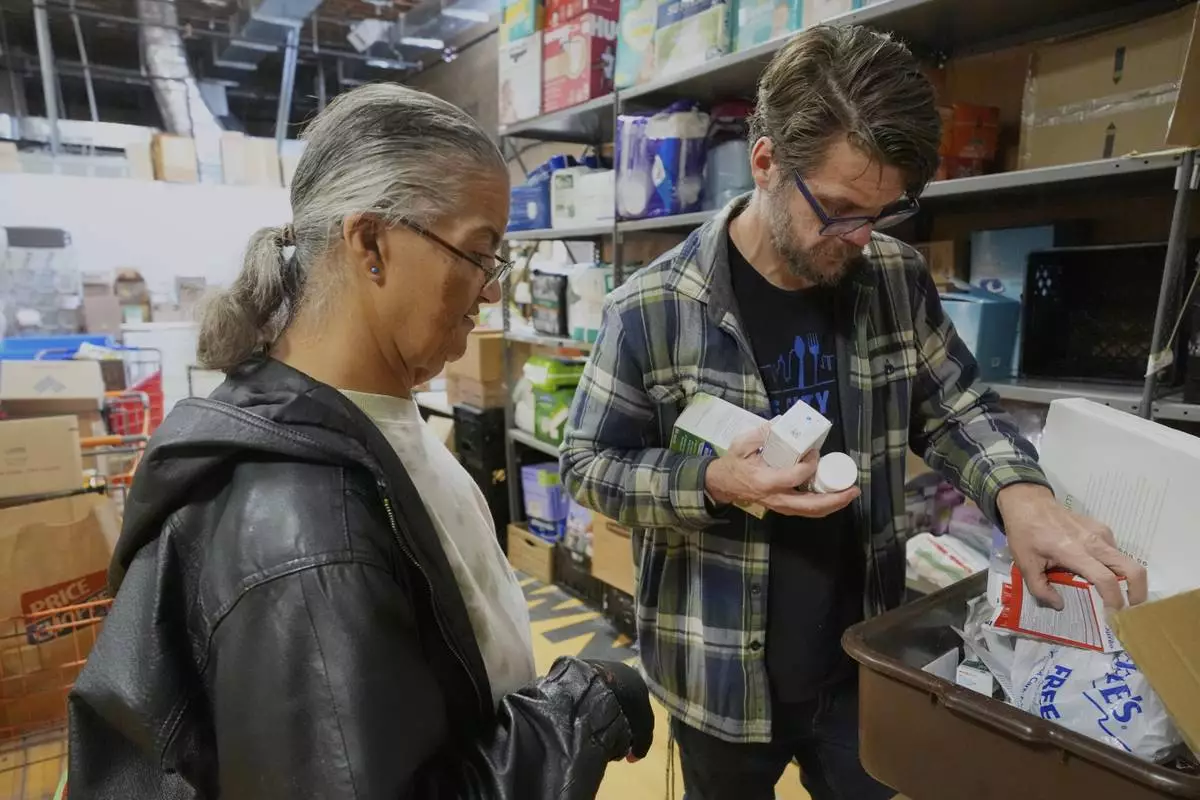 Pantry director Christopher Lowrance looks for items requested by Beth Anne Mollett, left, at the Bishop Sullivan Center food pantry, Tuesday, April 15, 2025, in Kansas City, Mo. (AP Photo/Charlie Riedel)