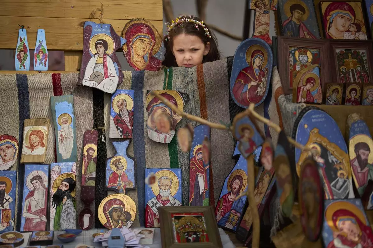 A child peers from behind a stand of an artist selling religious icons at a fair in Bucharest, Romania, April 5, 2025. (AP Photo/Vadim Ghirda)