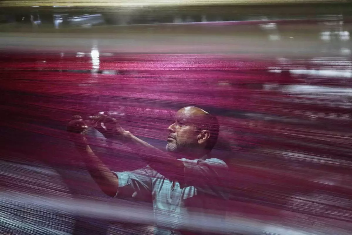 A textile worker checks thread reels on a carpet weaving machine at a factory, on the outskirts of Jammu, India, April 8, 2025. (AP Photo/Channi Anand)