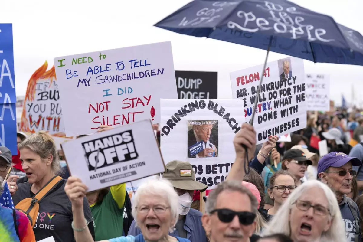 Demonstrators hold up signs during a "Hands Off!" protest against President Donald Trump at the Washington Monument in Washington, April 5, 2025. (AP Photo/Jose Luis Magana)