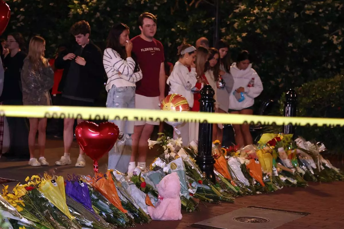 An impromptu memorial shared online brings students bearing flowers into the evening near the center of the Florida State campus in sight of the Student Union building, Tallahassee, Fla., Thursday, April 17, 2025. (AP Photo/Gary McCullough)