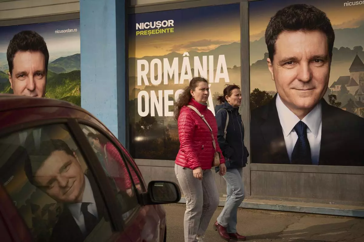 Women walk by posters of Nicusor Dan, the mayor of Bucharest and presidential candidate in the upcoming May elections in Bucharest, Romania, Friday, March 28, 2025. (AP Photo/Vadim Ghirda)