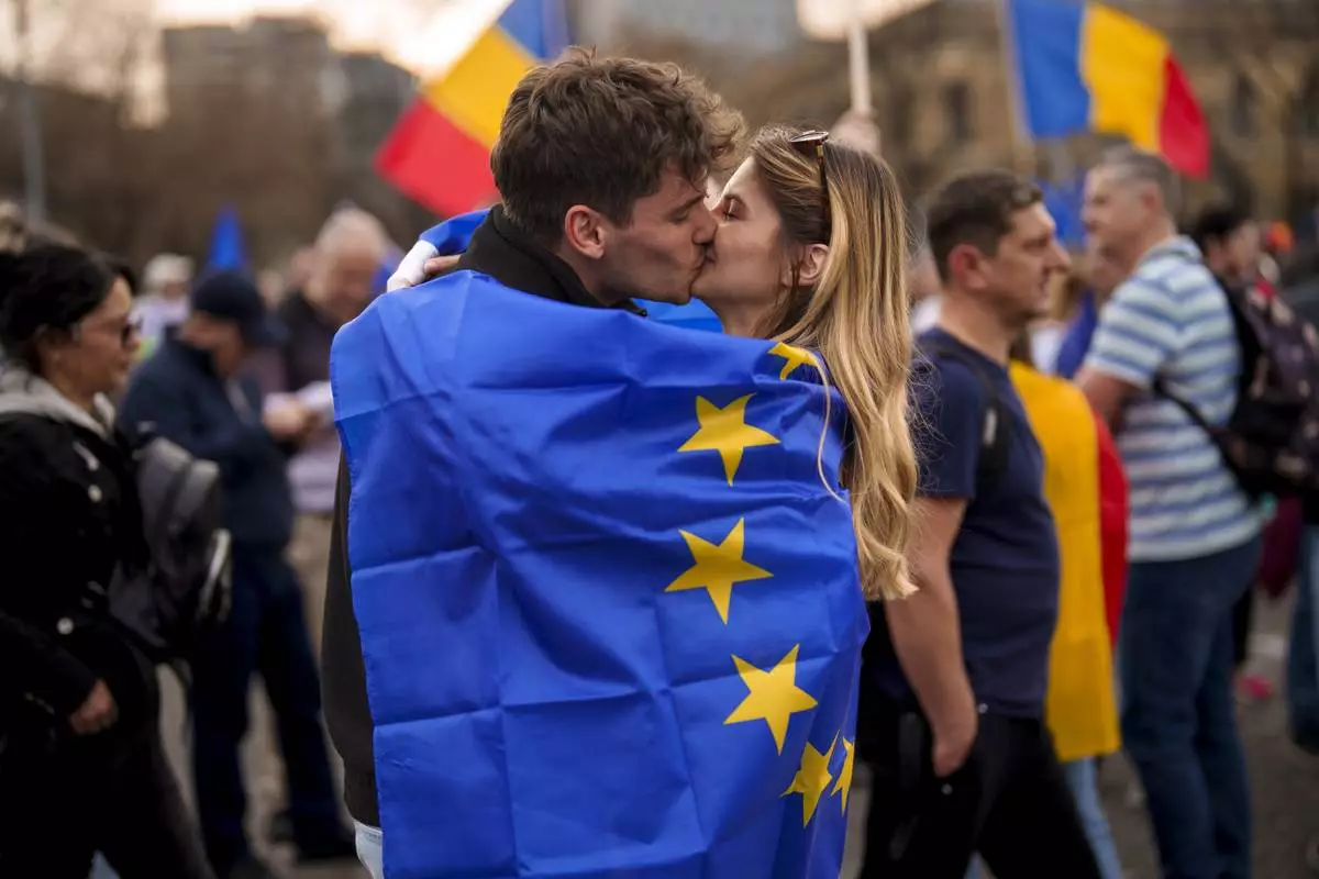 Young people kiss, wrapped in the European Union flag, at a pro-European rally, joined by thousands, to counter what the organizers described as a "wave of sovereignism and ultranationalism" in Bucharest, Romania, Saturday, March 15, 2025. (AP Photo/Vadim Ghirda)