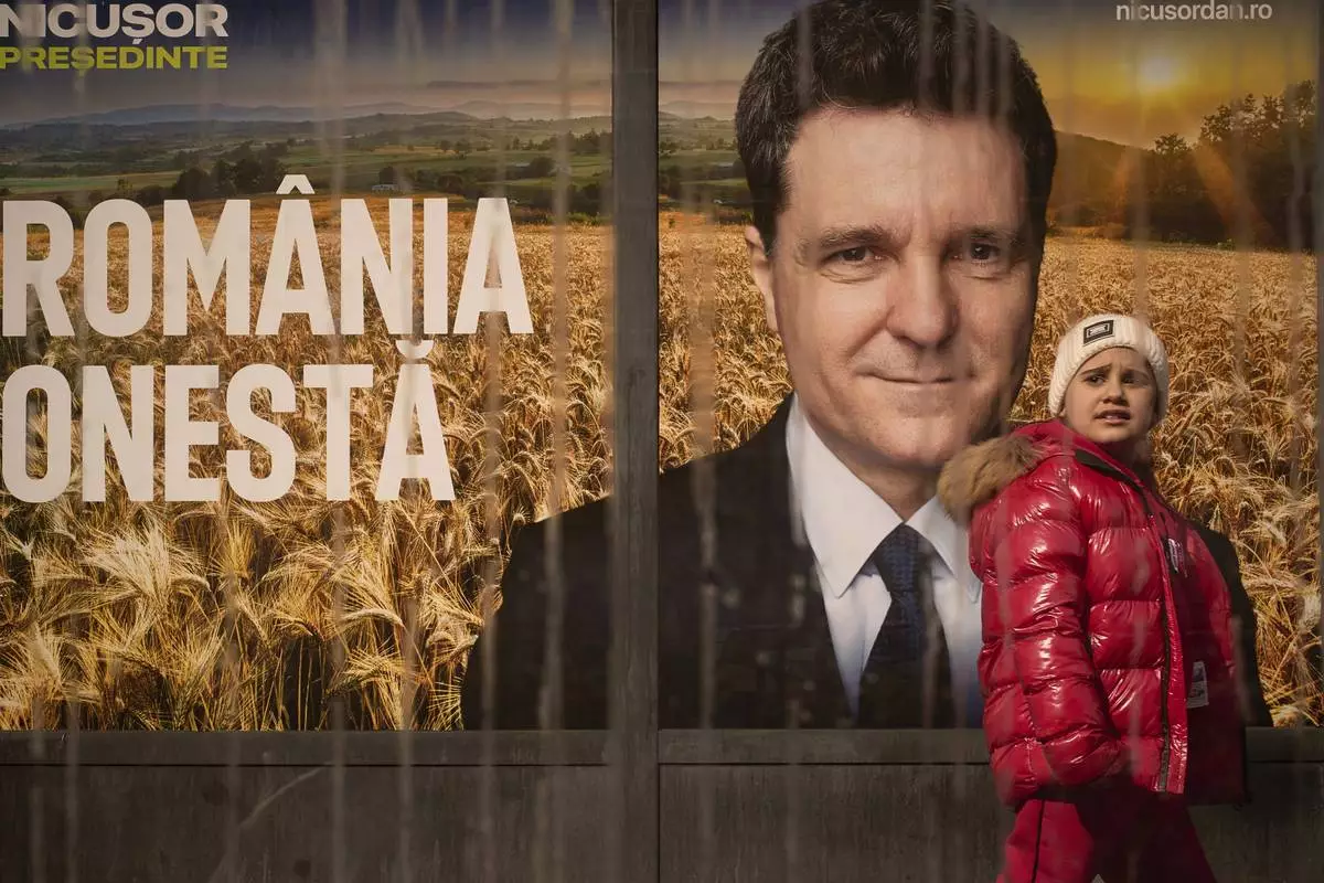 A child walks by a poster of Nicusor Dan, the mayor of Bucharest and presidential candidate in the upcoming May elections in Bucharest, Romania, Friday, March 28, 2025. (AP Photo/Vadim Ghirda)