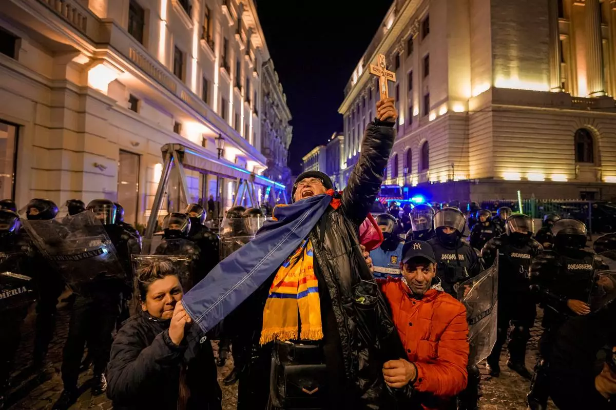 FILE - A woman screams holding a cross in front of riot policemen blocking a street following clashes with supporters of Calin Georgescu after Romania's electoral body rejected his candidacy in the presidential election rerun in Bucharest, Romania, Monday, March 10, 2025. (AP Photo/Andreea Alexandru, File)