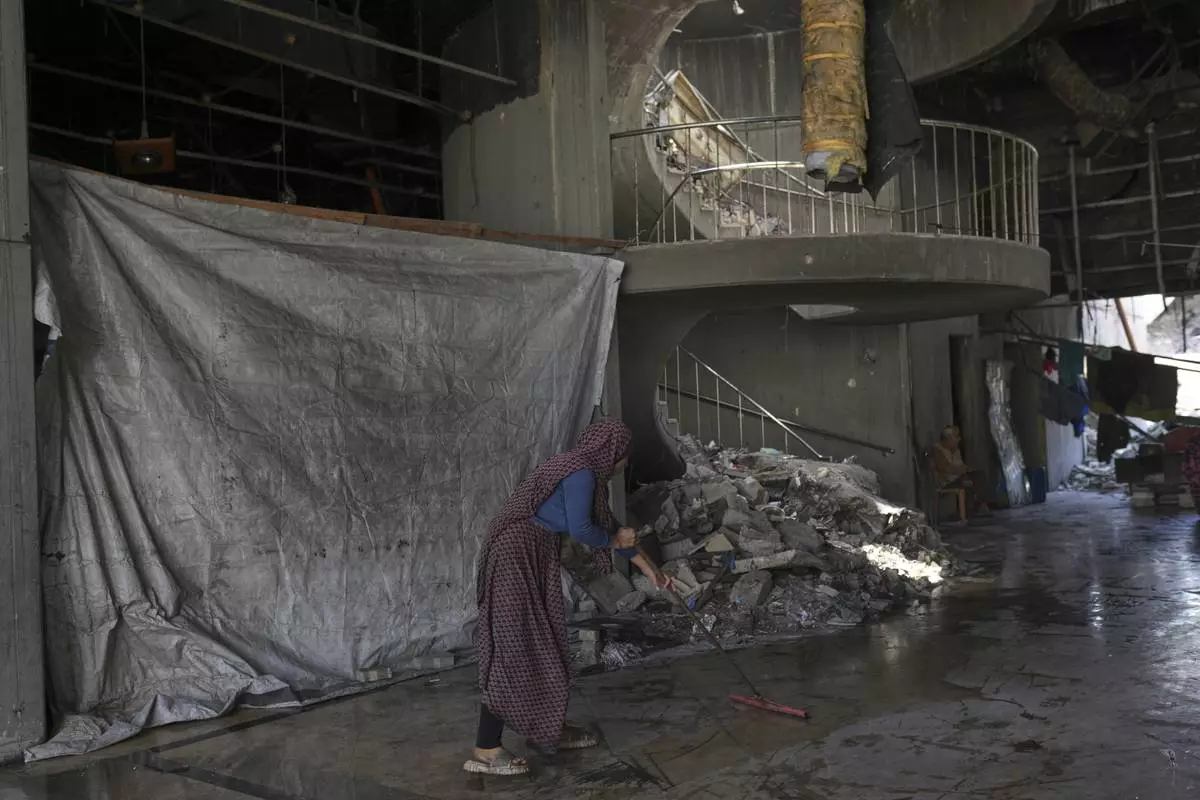 Karima Al-Kafarna cleans the hallway outside her family's makeshift home inside the destroyed Rashad Al-Shawa Cultural Center in Gaza City, Monday, April 21, 2025. (AP Photo/Jehad Alshrafi)