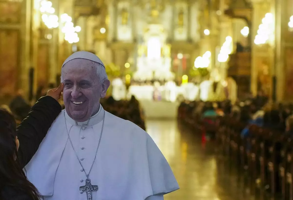 A woman reaches up to touch a life-size cutout of Pope Francis ahead of a Requiem Mass at the Cathedral in Santiago, Chile, Saturday, April 26, 2025. (AP Photo/Esteban Felix)
