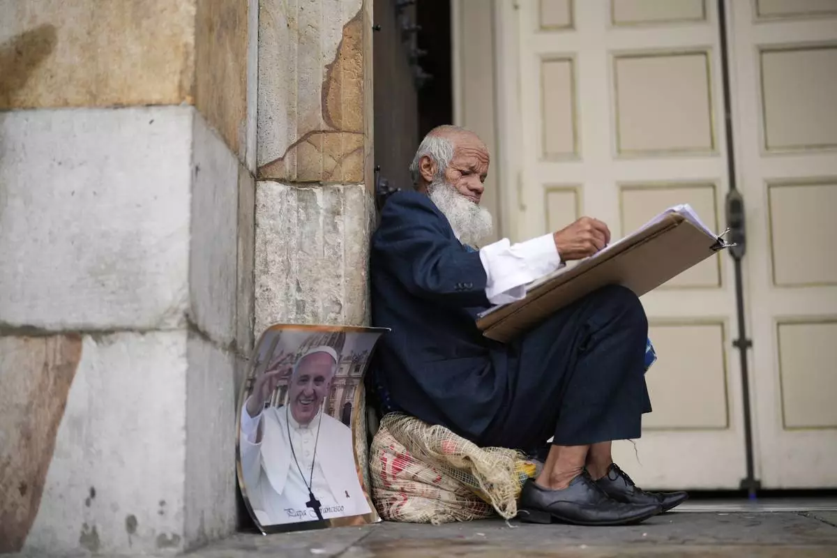 Oscar Gomez a street artist waits outside the Cathedral for a mass in tribute to the late Pope Francis in Bogota, Colombia, Saturday, April 26, 2025. (AP Photo/Fernando Vergara)
