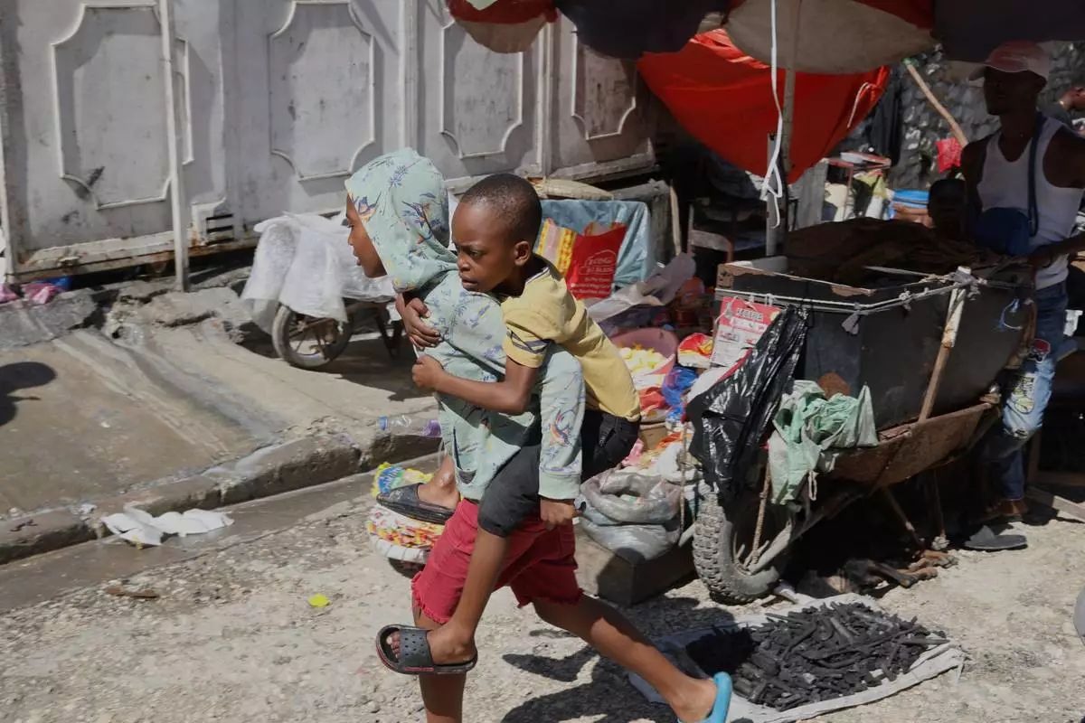 A youth carries a little boy on his back at a school that is now operating as a shelter for those fleeing their homes to escape gang violence in Port-au-Prince, Haiti, Monday, April 14, 2025. (AP Photo/Odelyn Joseph)