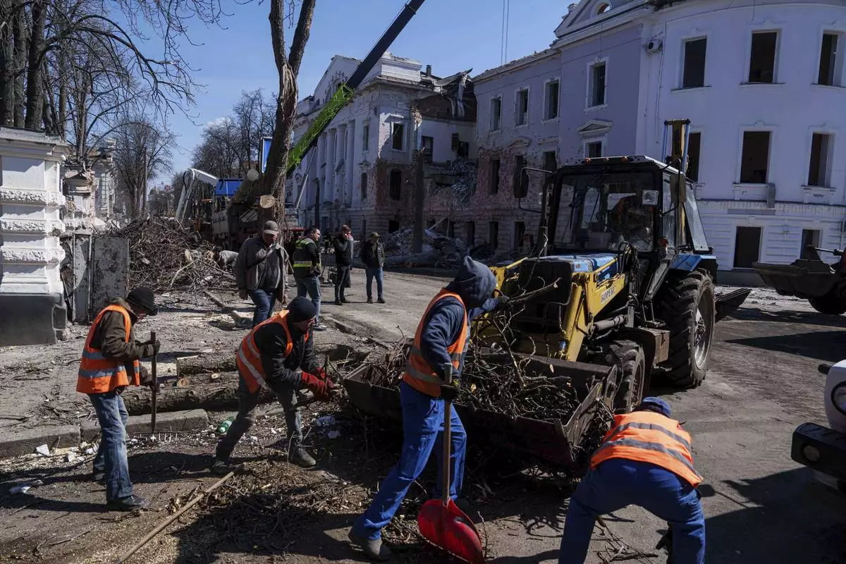 Municipal workers clean a street in front of a University building destroyed by a Russian missile strike in Sumy, Ukraine, Monday, April 14, 2025. (AP Photo/Evgeniy Maloletka)