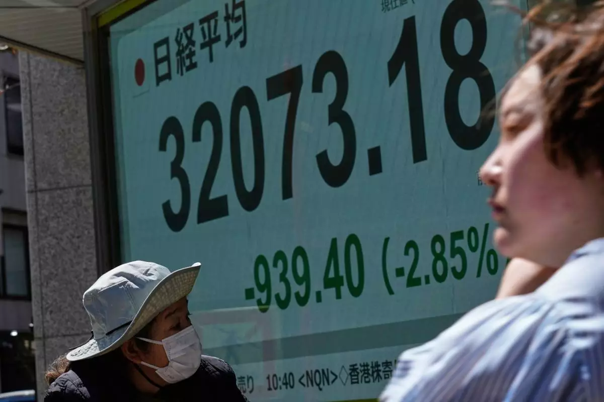 People walk past monitors showing Japan's Nikkei 225 index at a securities firm in Tokyo, Wednesday, April 9, 2025. (AP Photo/Hiro Komae)