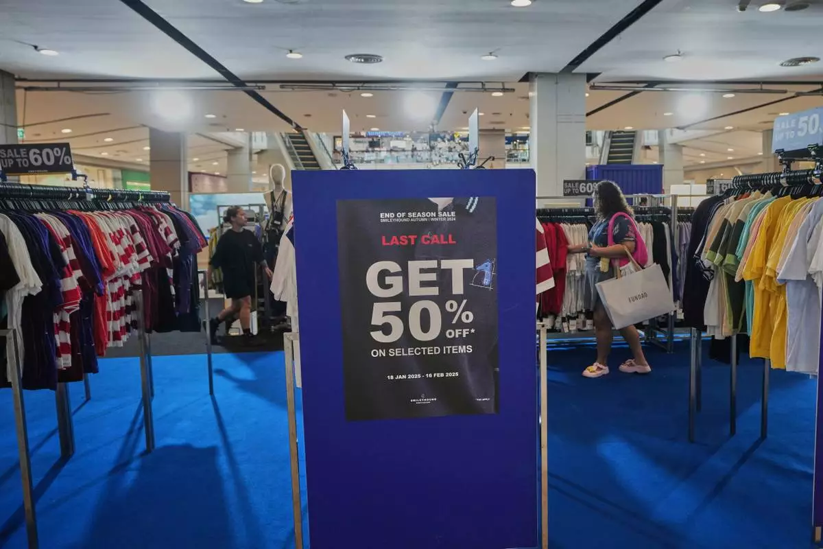 Shopper are seen behind a sales advertisement at a shopping mall in Bangkok, Thailand, Wednesday, April 9, 2025. (AP Photo/Sakchai Lalit)