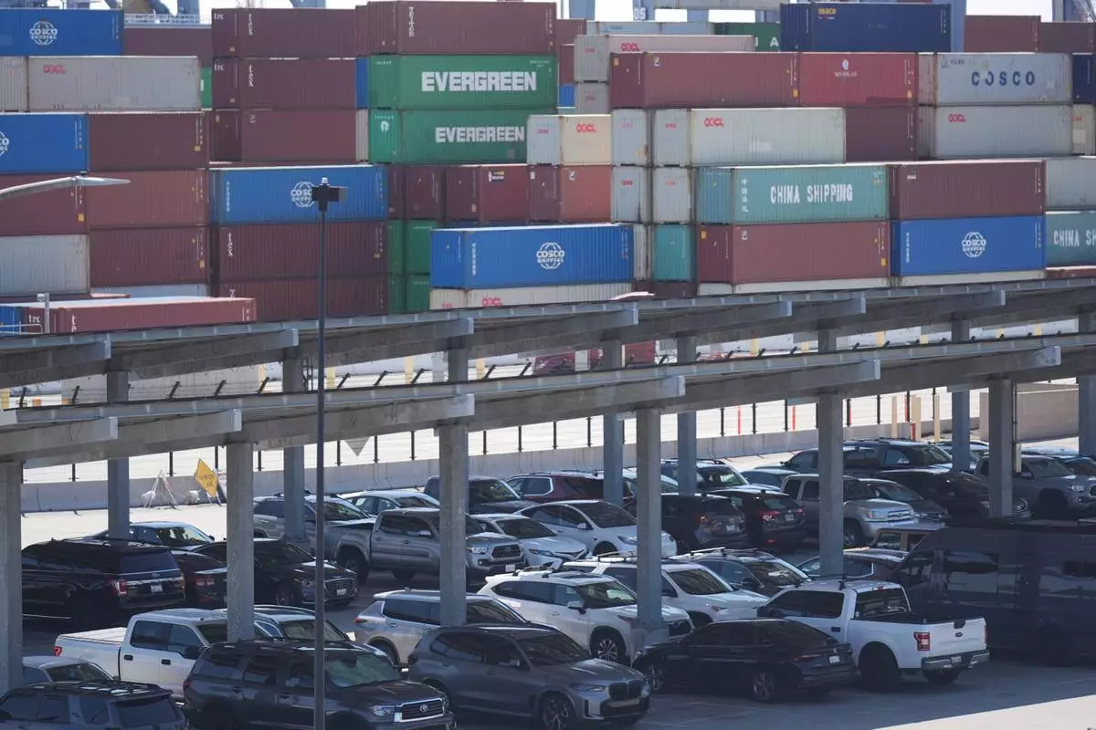 Vehicles are parked under solar panels as shipping containers sit stacked at the Long Beach Container Terminal in Long Beach, Calif., on Tuesday, April 8, 2025. (AP Photo/Damian Dovarganes)