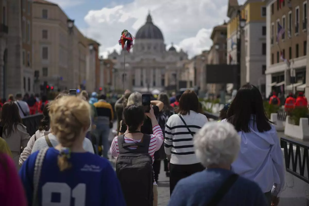 People walk along Via della Conciliazione avenue to line up to view Pope Francis lying in state inside St. Peter's Basilica, seen in the background, at the Vatican, Thursday, April 24, 2025. (AP Photo/Andrew Medichini)