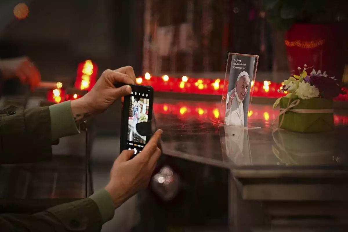 A woman takes a picture of a photograph of the late Pope Francis, that reads "Please, don't forget to pray for me" during a mass in his memory at the Chiesa di Santo Spirito in Sassia outside the Vatican, Thursday, April 24, 2025. (AP Photo/Andreea Alexandru)