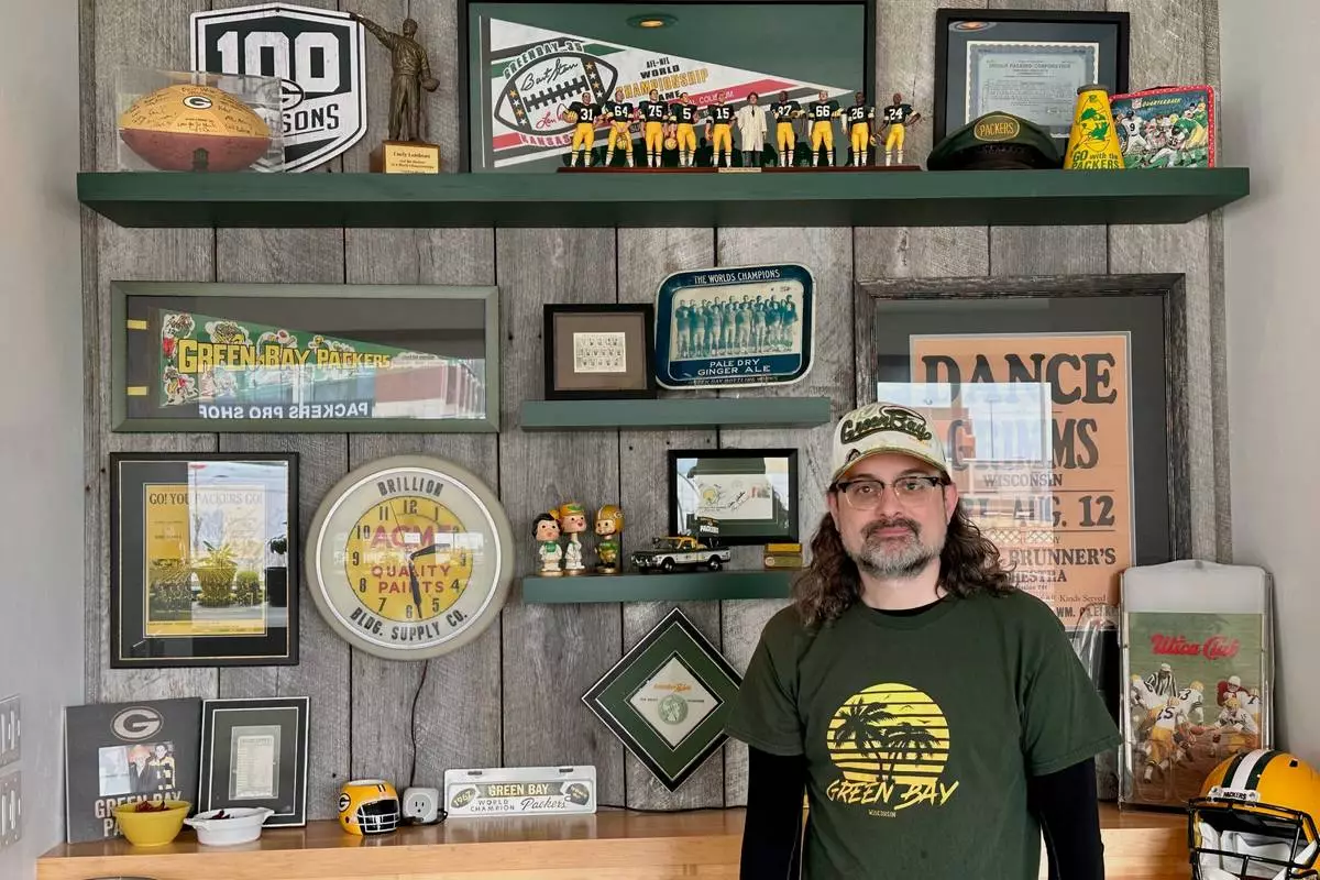 Corey Behnke, who lives across the street from Lambeau Field, stands in front of some of the Green Bay Packers memorabilia he has collected on Thursday, April 17, 2025 in Green Bay, Wis. (AP Photo/Stephen Megargee)