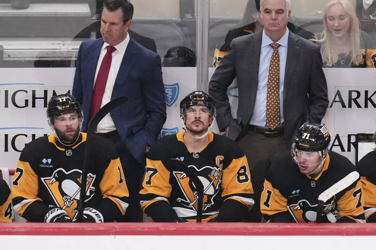 Pittsburgh Penguins' Bryan Rust (17), Sidney Crosby (87), and Evgeni Malkin (71) sit on the bench in front of head coach Mike Sullivan, left rear, and assistant coach Mike Vellucci during the third period of an NHL hockey game against the Boston Bruins in Pittsburgh, Sunday, April 13, 2025. (AP Photo/Gene J. Puskar)