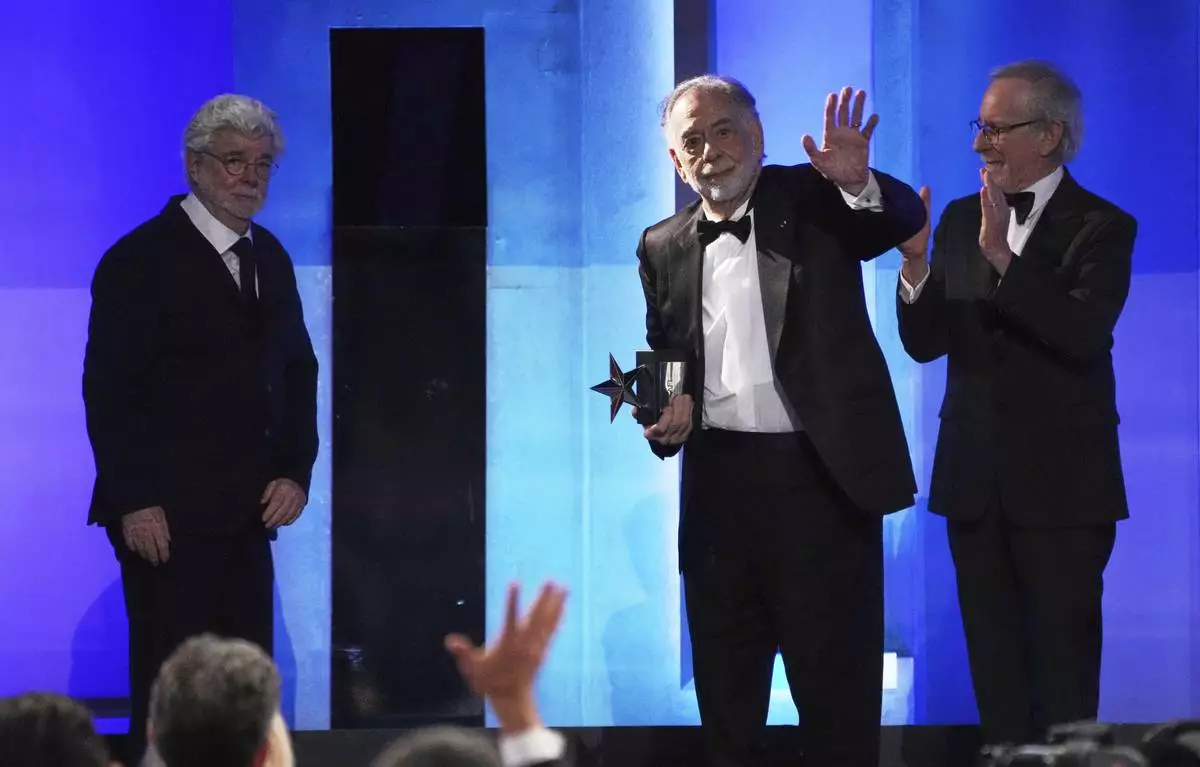 Francis Ford Coppola, second from right, waves to the audience as presenters George Lucas, left, and Steven Spielberg look on during the 50th AFI Life Achievement Award tribute to Coppola on Saturday, April 26, 2025, at the Dolby Theatre in Los Angeles. (AP Photo/Chris Pizzello)