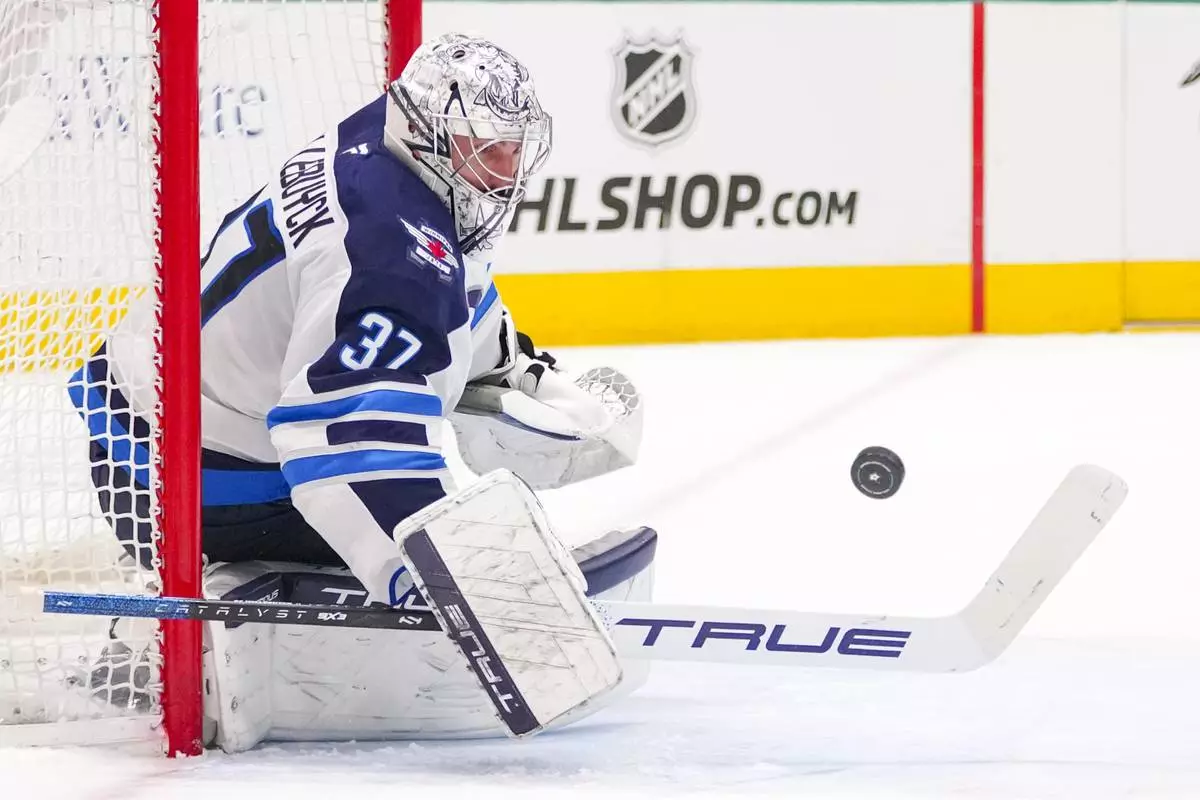Winnipeg Jets goaltender Connor Hellebuyck blocks a shot by the Dallas Stars during the first period of an NHL hockey game Thursday, April 10, 2025, in Dallas. (AP Photo/Julio Cortez)