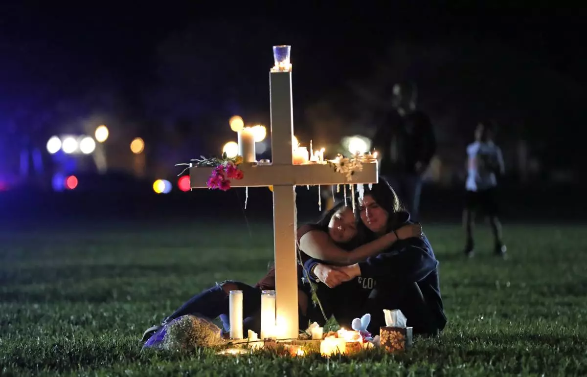 FILE - People comfort each other as they sit and mourn at one of seventeen crosses, Feb. 15, 2018, after a candlelight vigil for the victims of the shooting at Marjory Stoneman Douglas High School, in Parkland, Fla. (AP Photo/Gerald Herbert, File)