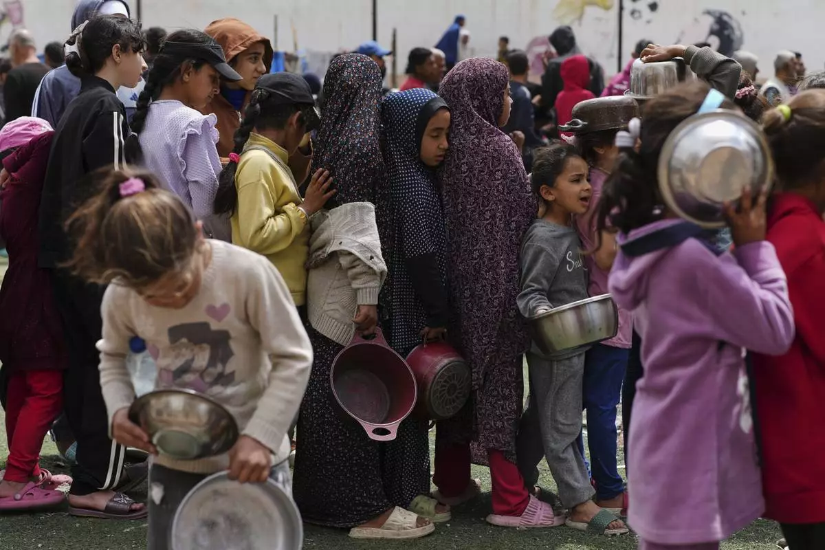 Palestinians wait for donated food at a distribution center in Nuseirat, central Gaza Strip, Friday, April 11, 2025. (AP Photo/Abdel Kareem Hana)