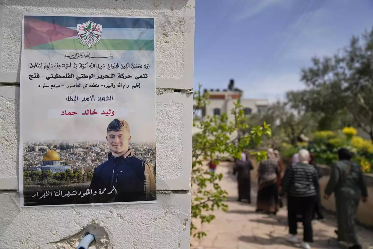 Palestinian women walk past a poster showing Waleed Ahmad that reads in Arabic, "The hero prisoner Martyr, mercy and eternity for our righteous Martyrs," in the West Bank town of Silwad, northeast of Ramallah, Wednesday, March 26, 2025. (AP Photo/Nasser Nasser)