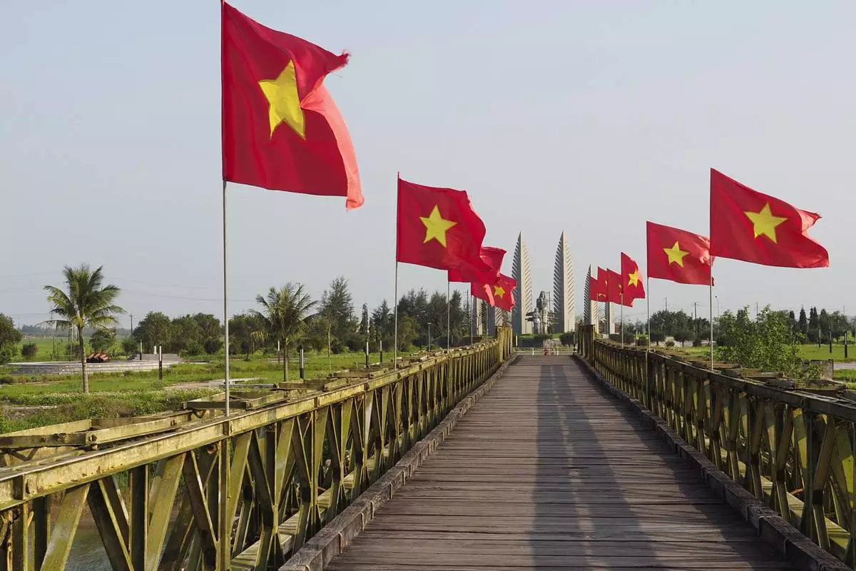 Vietnamese flags fly on the Hien Luong Bridge, with a memorial in the distance, at the former border between North and South Vietnam, Quang Tri province, Feb. 22, 2024. (AP Photo/David Rising)