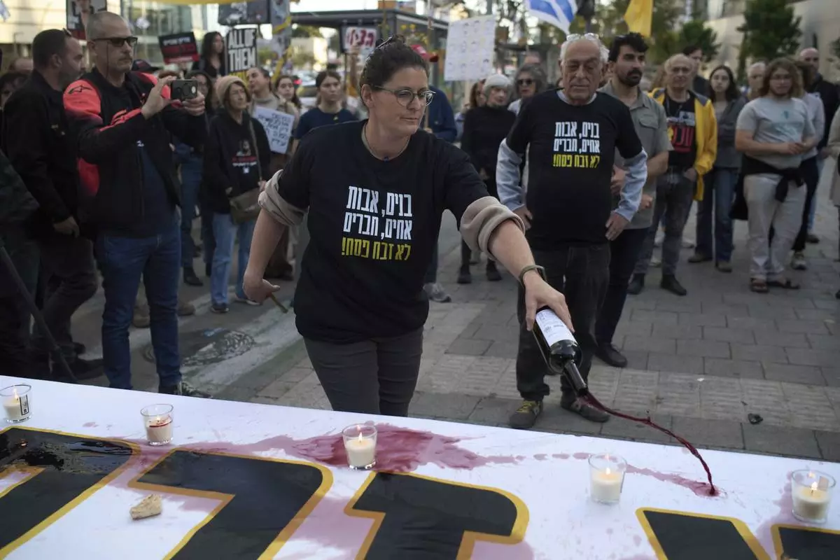 A relative of a hostage held in the Gaza Strip pours wine over a table as she takes part in a protest demanding immediate release of the hostages from Hamas captivity, during the Jewish holiday of Passover, in Tel Aviv, Israel, Saturday, April 12, 2025. (AP Photo/Leo Correa)