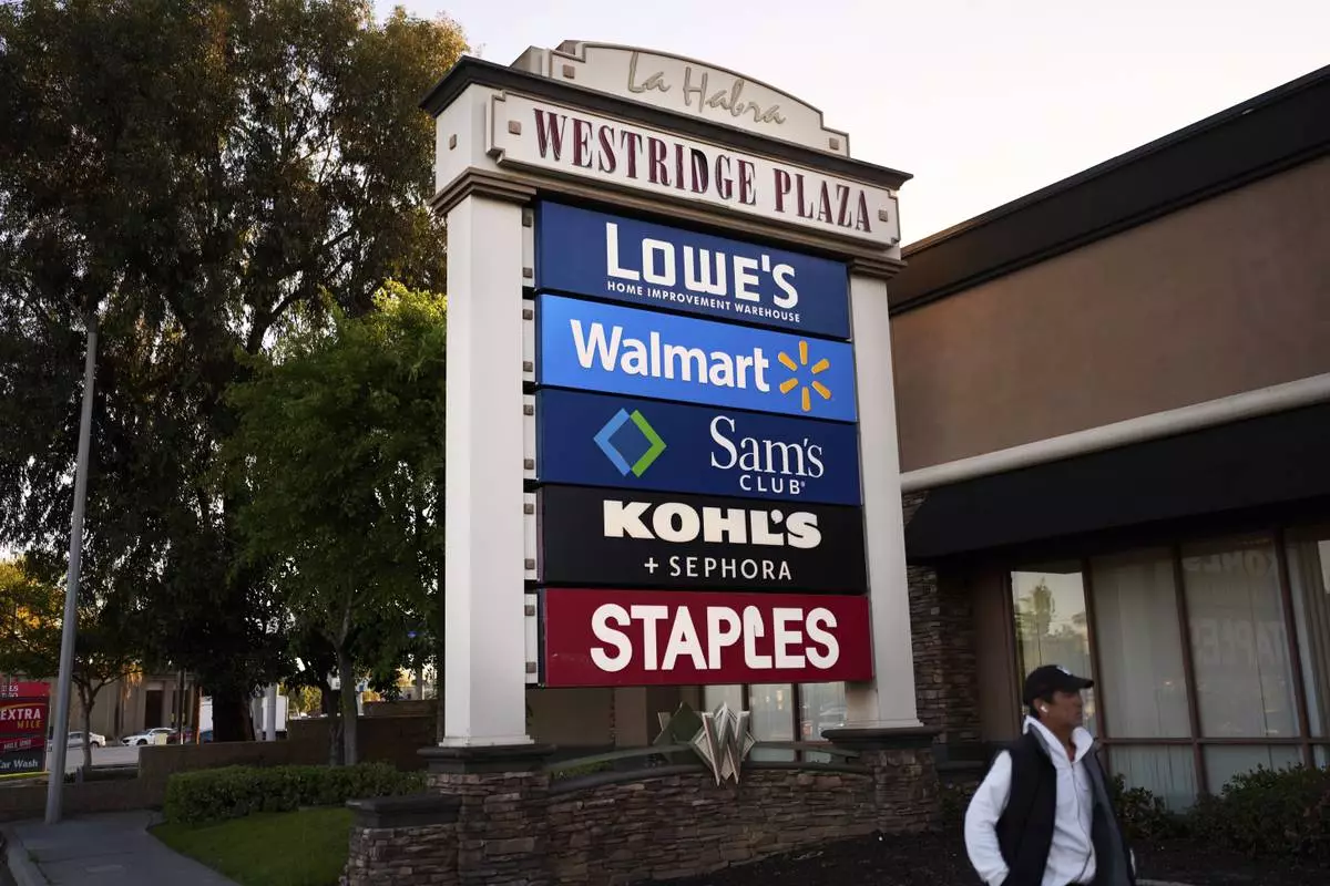 A person walks past a cluster of retail store signs in La Habra, Calif., Wednesday, April 2, 2025. (AP Photo/Jae C. Hong)