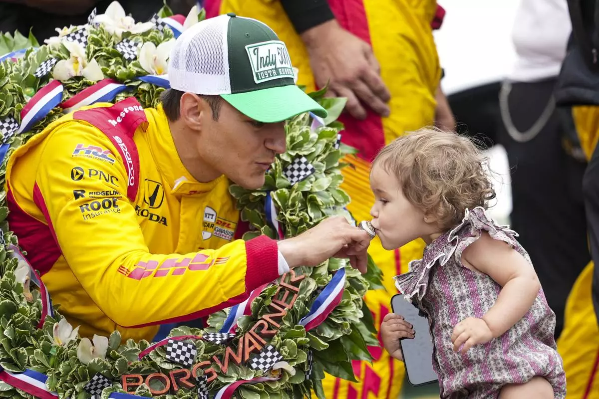 Alex Palou, left, of Spain, has his winner's ring kissed by his daughter Lucia on the Yard of Bricks on the start/finish line after winning the Indianapolis 500 auto race at Indianapolis Motor Speedway in Indianapolis, Sunday, May 25, 2025. (AP Photo/AJ Mast)
