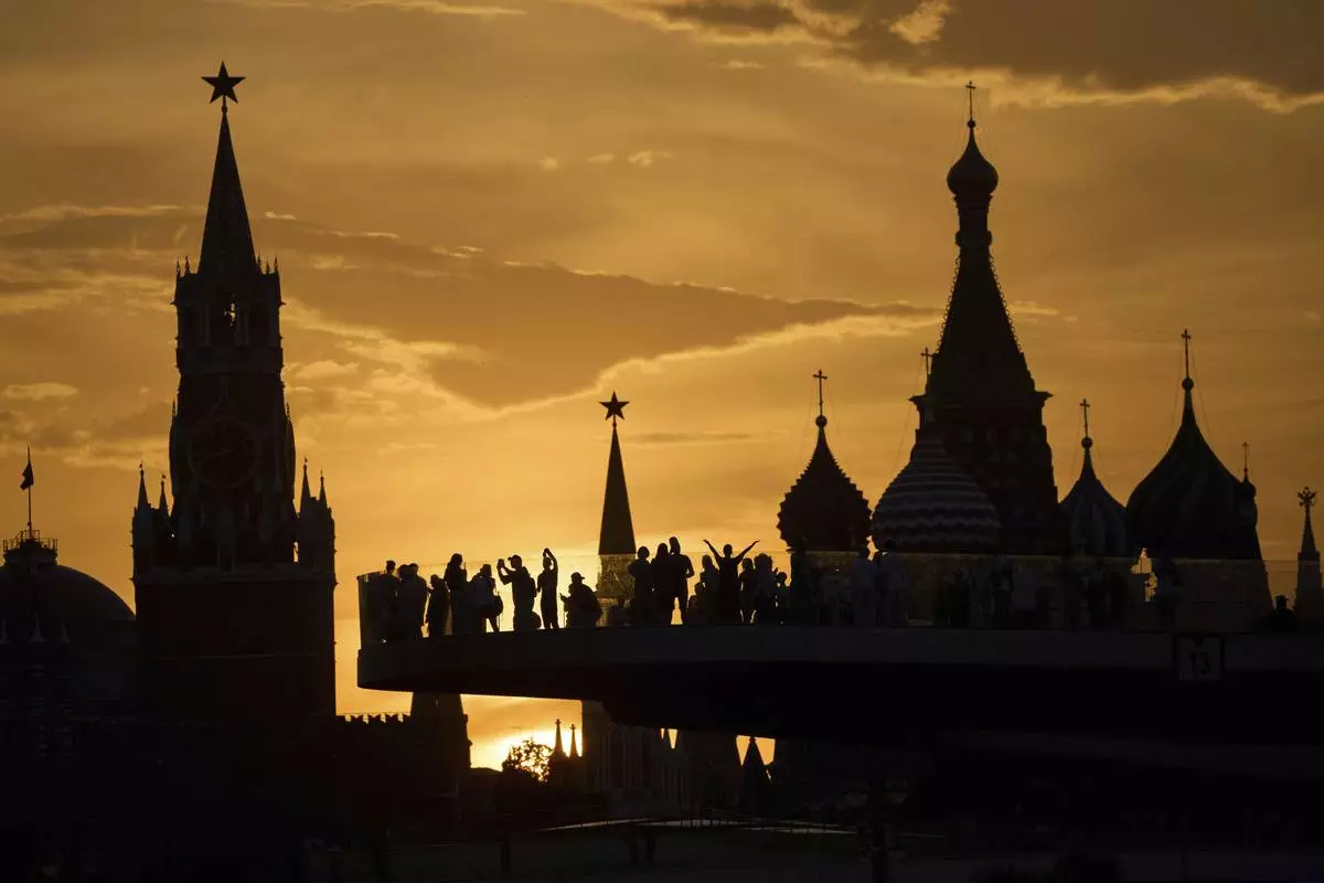 People watch and photograph sunset behind the Kremlin standing on the "Flying glass bridge" over the Moscow River at Zaryadye park in Moscow, Russia, Thursday, May 29, 2025. (AP Photo/Alexander Zemlianichenko)