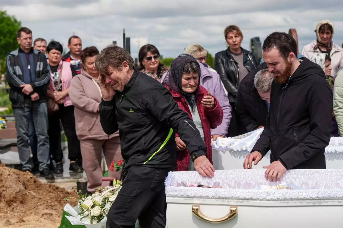 A father, left, mourns his children Tamara Martyniuk, 8, Stanislav Martyniuk, 12, and Roman Martyniuk, 17, killed in a Russian strike on Sunday, during farewell ceremony in Korostyshiv, Zhytomyr region, Ukraine, Wednesday, May 28, 2025. (AP Photo/Evgeniy Maloletka)