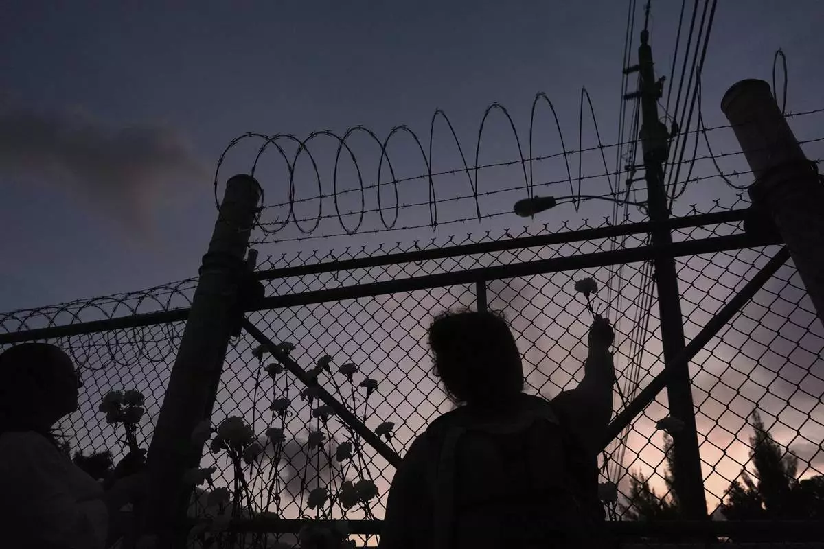 People place flowers on a fence outside Krome Detention Center in Miami, Saturday, May 24, 2025, during a vigil to recognize people who have died in U.S. Immigration and Customs Enforcement custody as well as those affected by mass deportations. (AP Photo/Rebecca Blackwell)