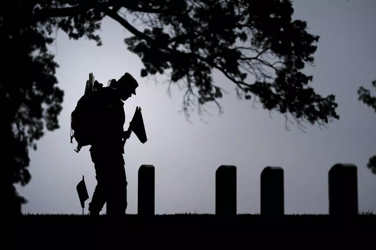 A member of the 3rd U.S. Infantry Regiment places flags at the headstones of service members buried at Arlington National Cemetery, ahead of Memorial Day, Thursday, May 22, 2025, in Arlington, Va. (AP Photo/Julia Demaree Nikhinson)