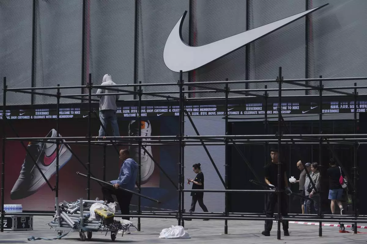 Shoppers walk by as workers install a platform near a Nike store outside a shopping mall in Beijing, Sunday, May 11, 2025. (AP Photo/Andy Wong)