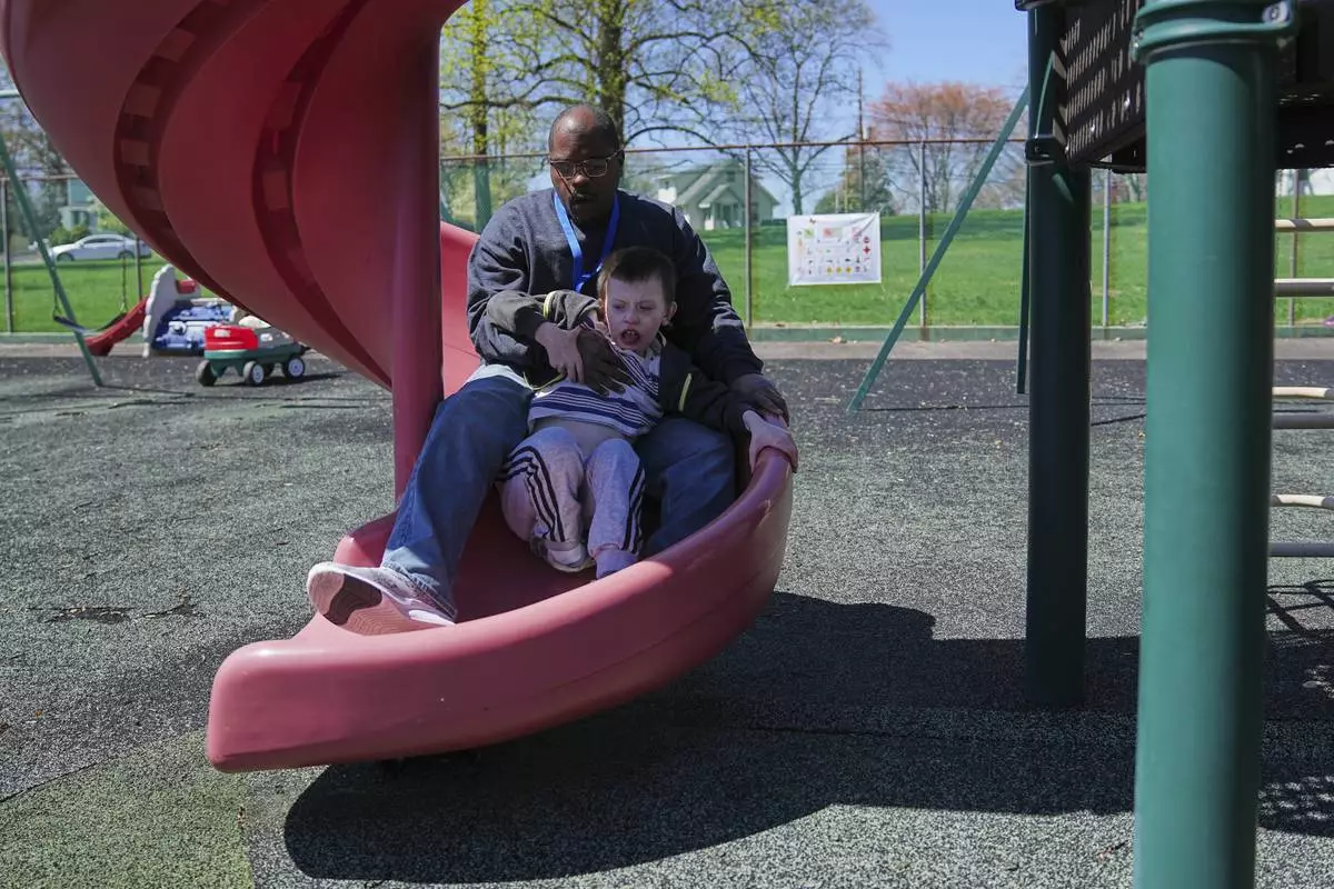 Mark takes a ride on a slide with paraprofessional Raheem Morton at Archbishop Damiano School in Westville, N.J., Wednesday, April 9, 2025. (AP Photo/Matt Rourke)