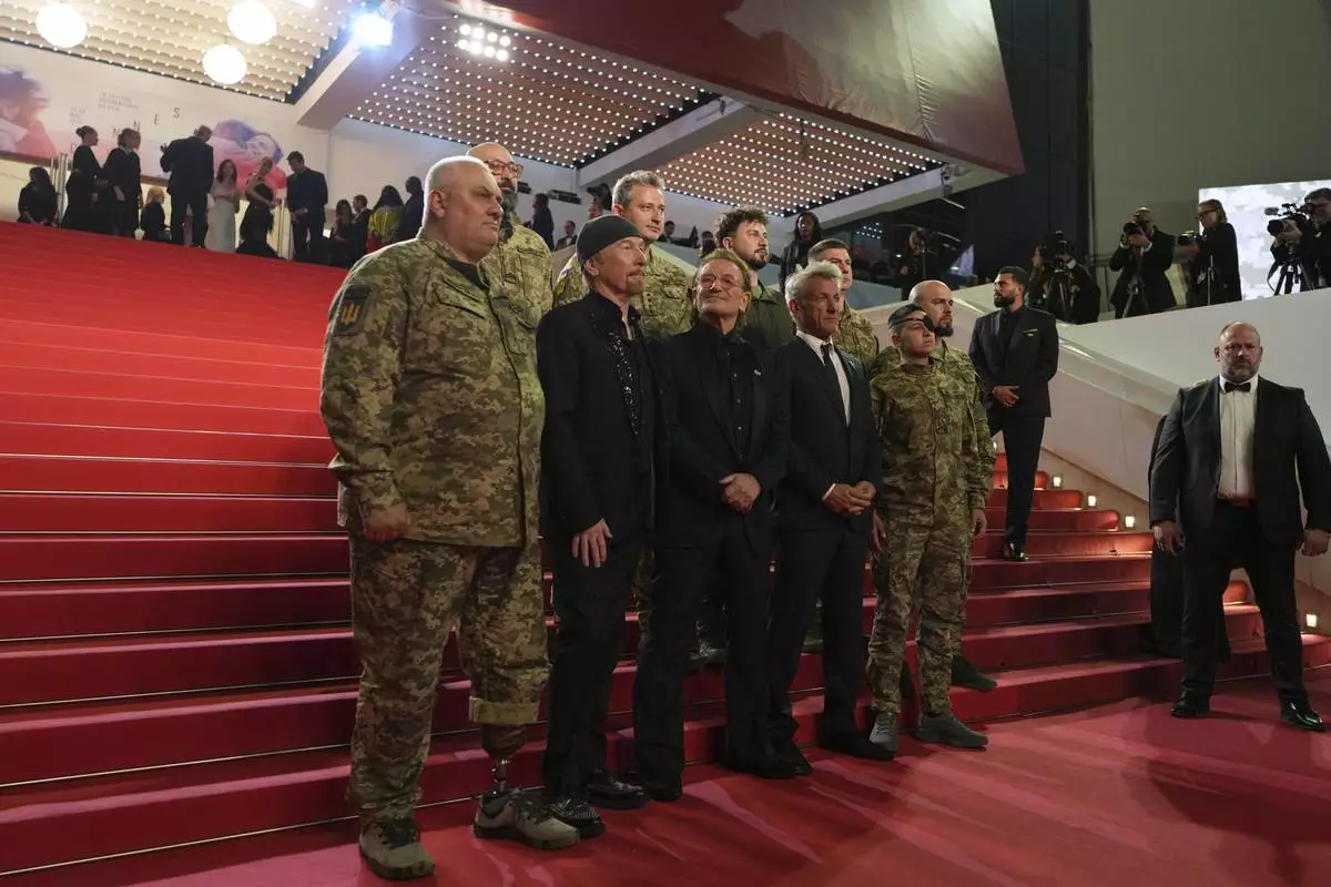 The Edge, from second left, Bono and Sean Penn pose with military personnel for photographers upon arrival at the premiere of the film 'Bono: Stories of Surrender' at the 78th international film festival, Cannes, southern France, Friday, May 16, 2025. (AP Photo/Natacha Pisarenko)