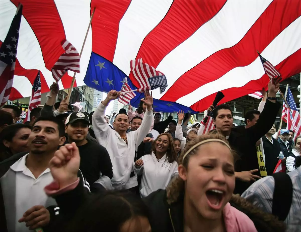 FILE - Participants in an immigration rights rally walk under a giant American flag during a march through downtown Chicago, May 1, 2006. (AP Photo/M. Spencer Green, File)