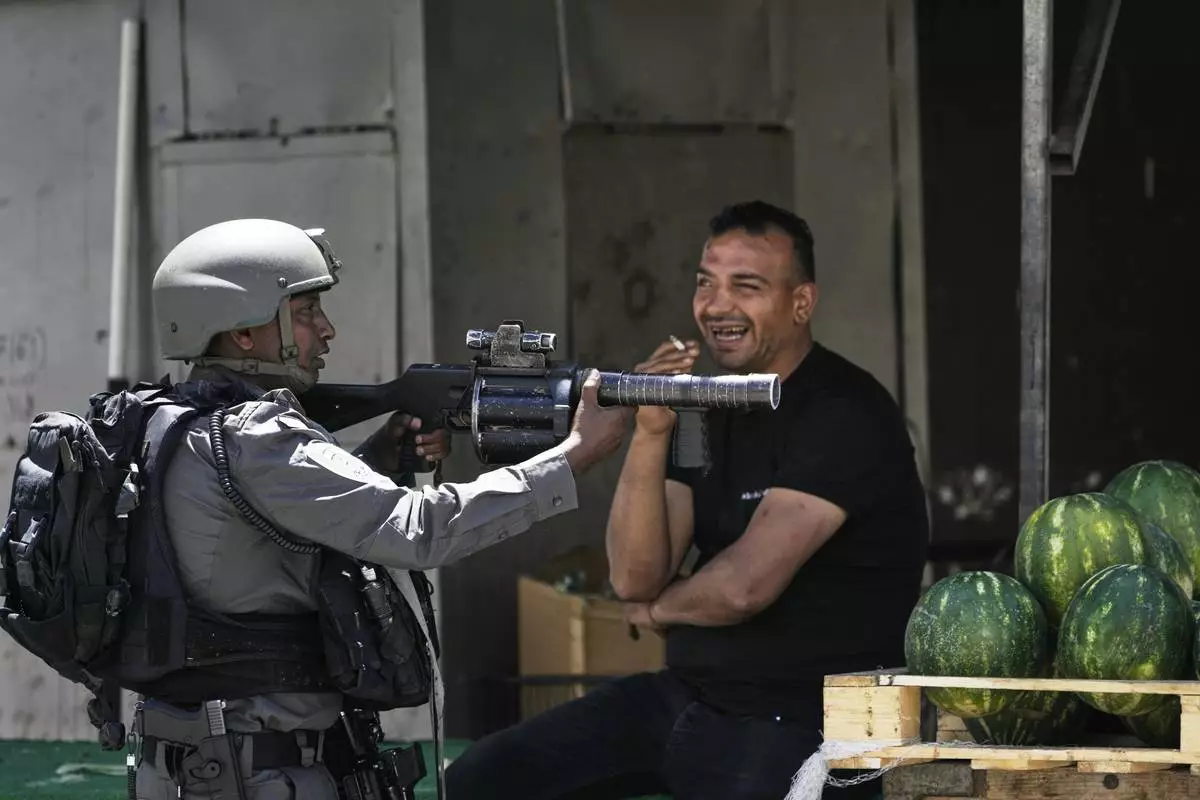 An Israeli border police officer takes up position next to a watermelon vendor, during a military raid in the Askar refugee camp near the West Bank city of Nablus, Tuesday, May 20, 2025. (AP Photo/Majdi Muhammad)