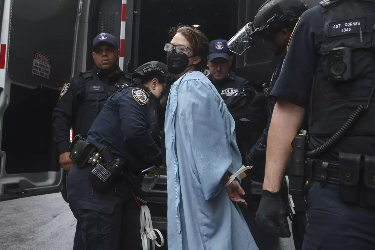 A person wearing graduate robes is detained by police across the street from the main gates of Columbia University, Wednesday, May 21, 2025, in New York. (AP Photo/Heather Khalifa)