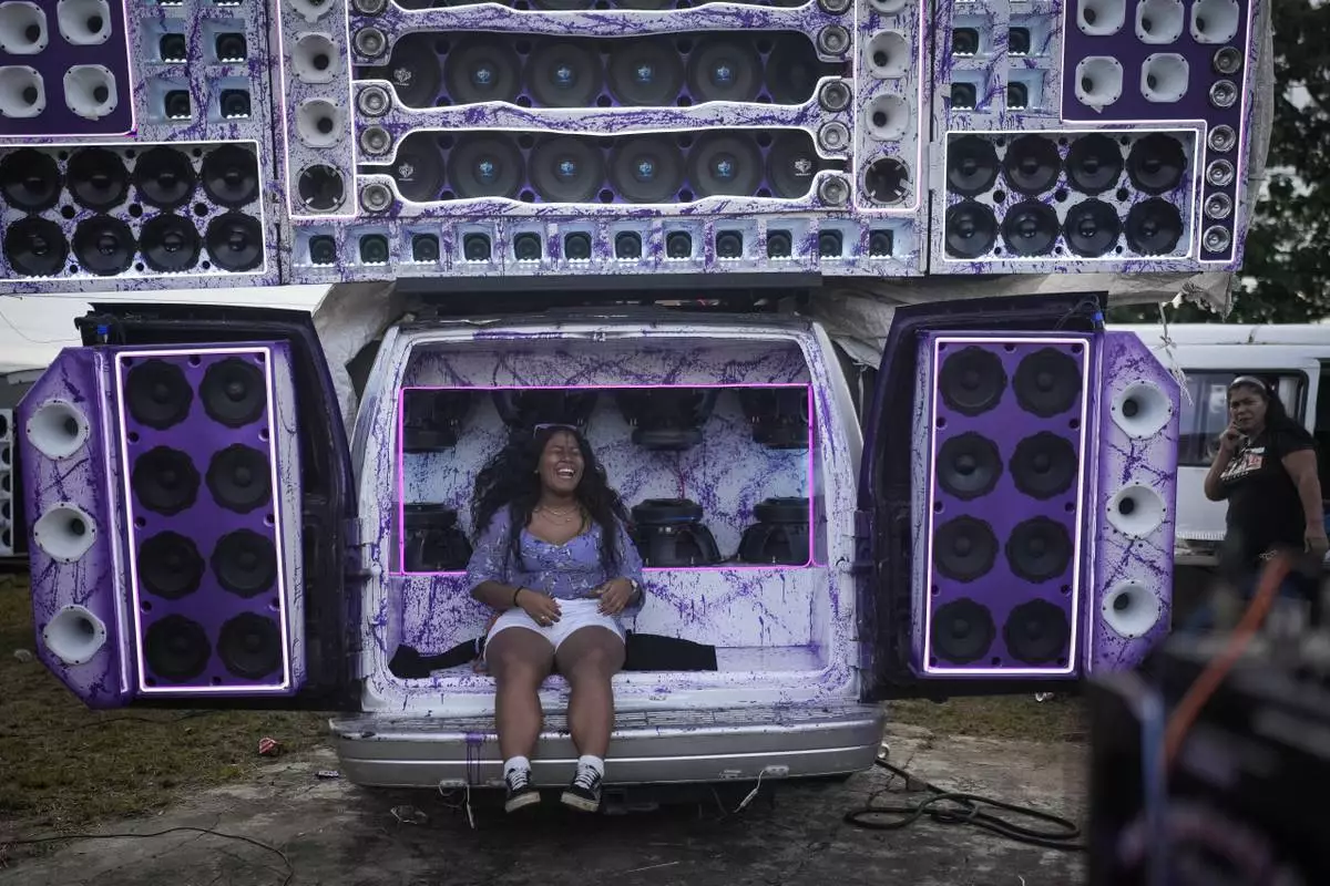 A woman sits on speakers playing music during a Red Devils bus exhibition in La Chorrera, Panama, Sunday, June 30, 2024. (AP Photo/Matias Delacroix)