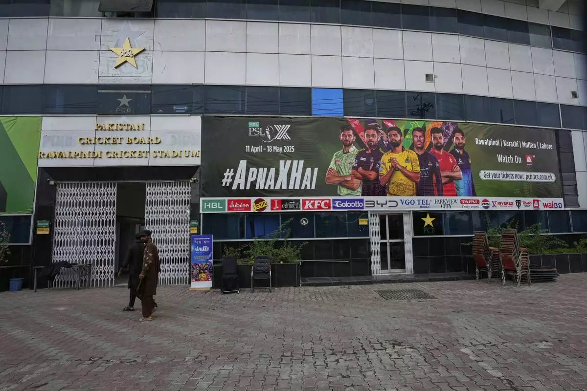 Workers walk past an advertisement board of Pakistan Super League Twenty20 tournament with the pictures of cricketers, installed at the Rawalpindi Cricket Stadium, in Rawalpindi, Pakistan, Friday, May 9, 2025. (AP Photo/Anjum Naveed)