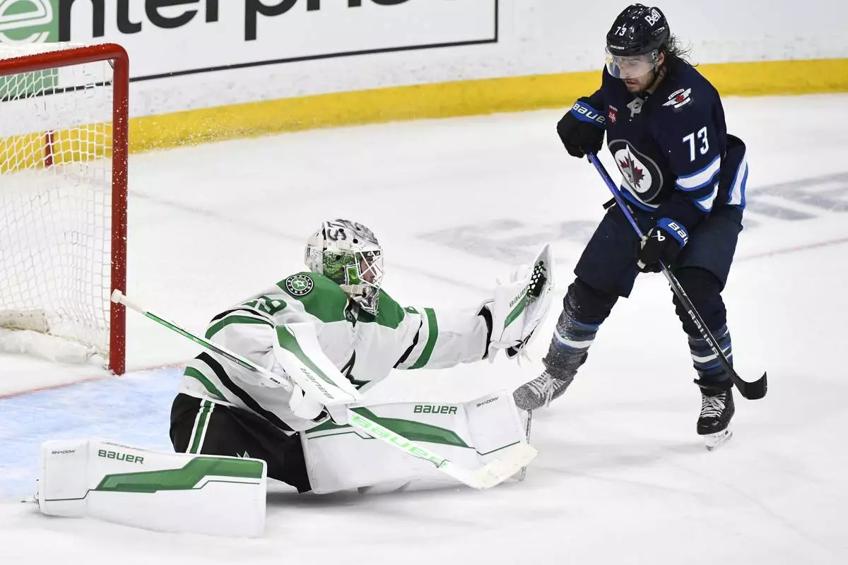 Dallas Stars goaltender Jake Oettinger (29) makes a save on a Winnipeg Jets shot as Brandon Tanev (73) looks for the rebound during third period NHL playoff hockey action in Winnipeg, Thursday, May 15, 2025. (Fred Greenslade/The Canadian Press via AP)